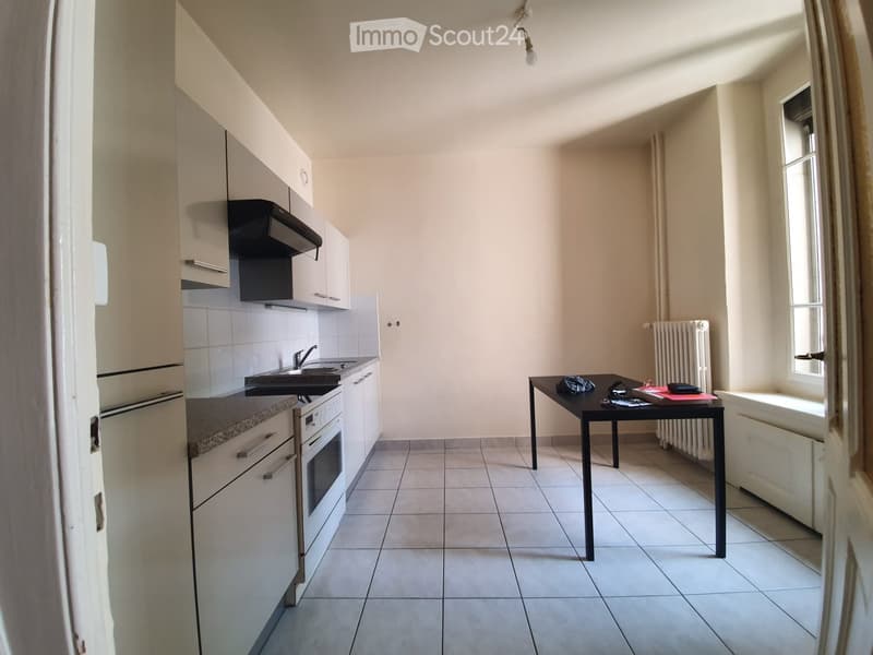 Modern kitchen with white cabinets, stainless steel appliances, tiled floor, and a small dining table with items on it.