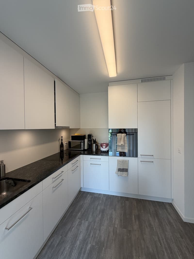 Modern kitchen with white cabinets, dark countertops, and stainless steel appliances. Features a sink, microwave, coffee maker, and oven.