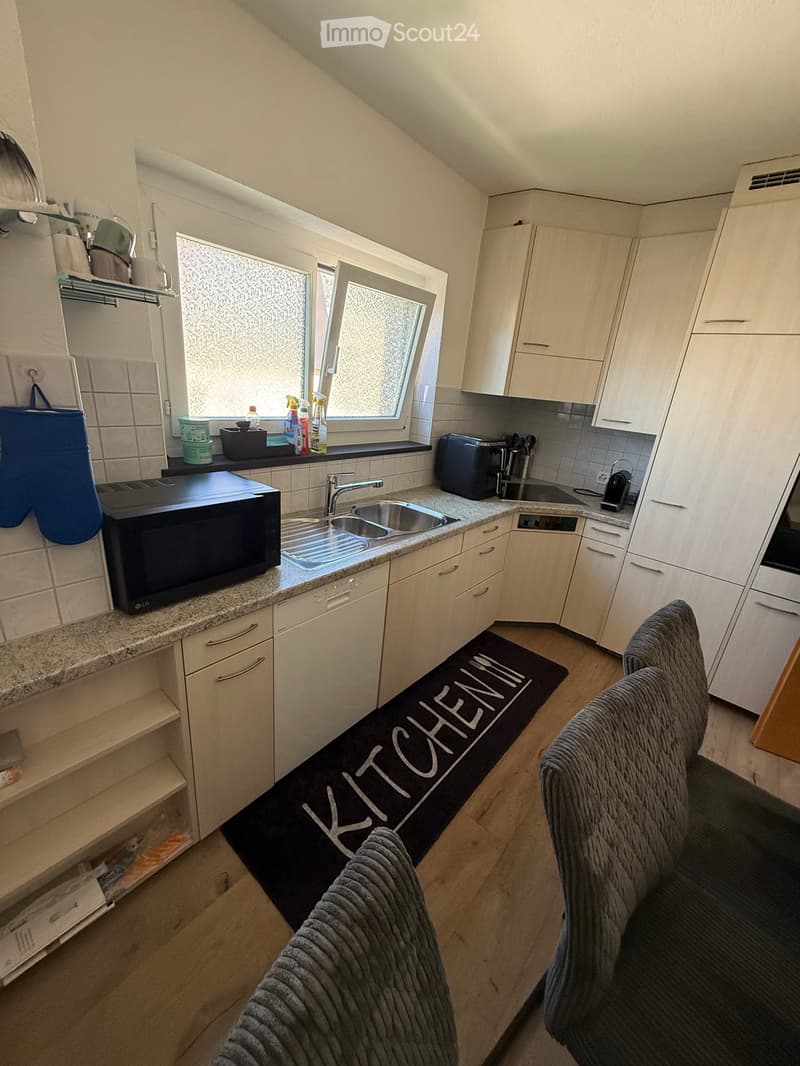 Modern kitchen with white cabinets, granite countertops, stainless steel sink, microwave, toaster, coffee maker, and a small seating area with a couch and blanket.