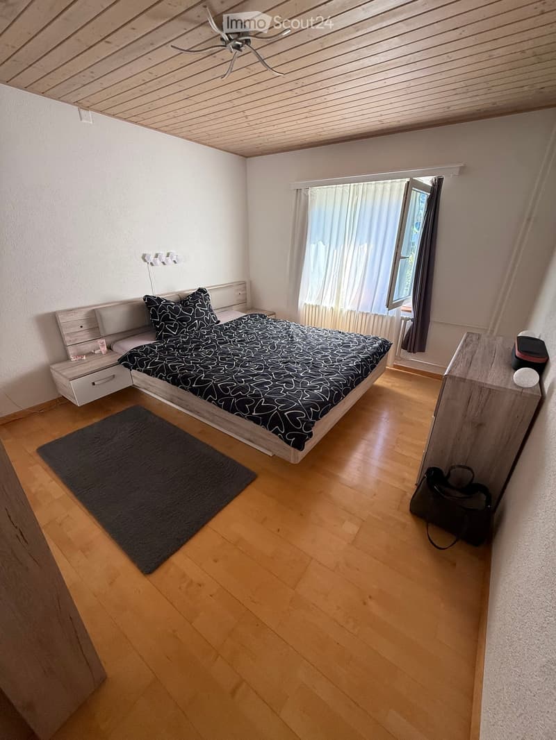 Cozy bedroom with wooden flooring, a bed with black and white bedding, a nightstand, a rug, and a handbag on the floor.
