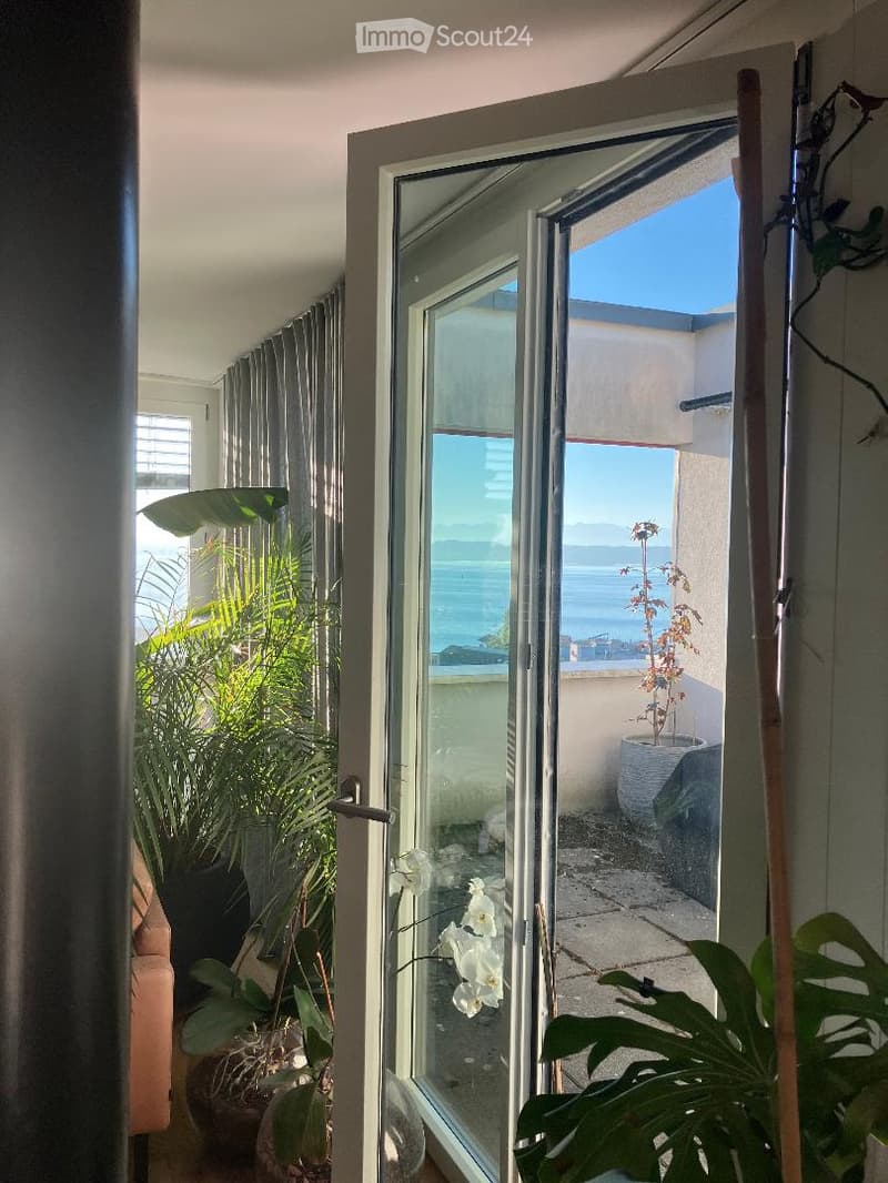 Open sliding glass door leading to a balcony with ocean view, potted plants, and a small seating area.