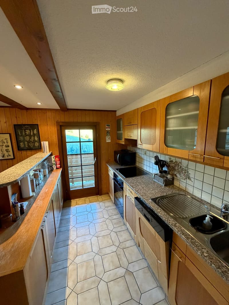 Bright kitchen with wooden cabinets, granite countertops, and a sink. Features include a microwave, oven, and a framed picture on the wall. The space has a door leading outside.
