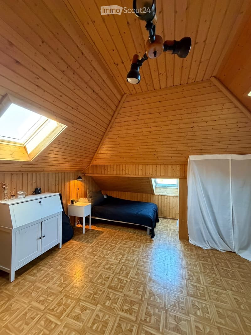 Cozy attic bedroom with wooden walls and slanted ceilings, featuring a bed, nightstand, and cabinet.