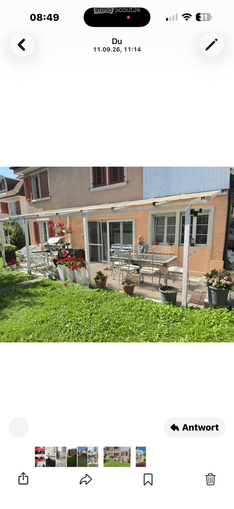 Outdoor patio area with a dining set, grill, potted plants, and a well-maintained lawn in front of a house with shutters and a covered terrace.
