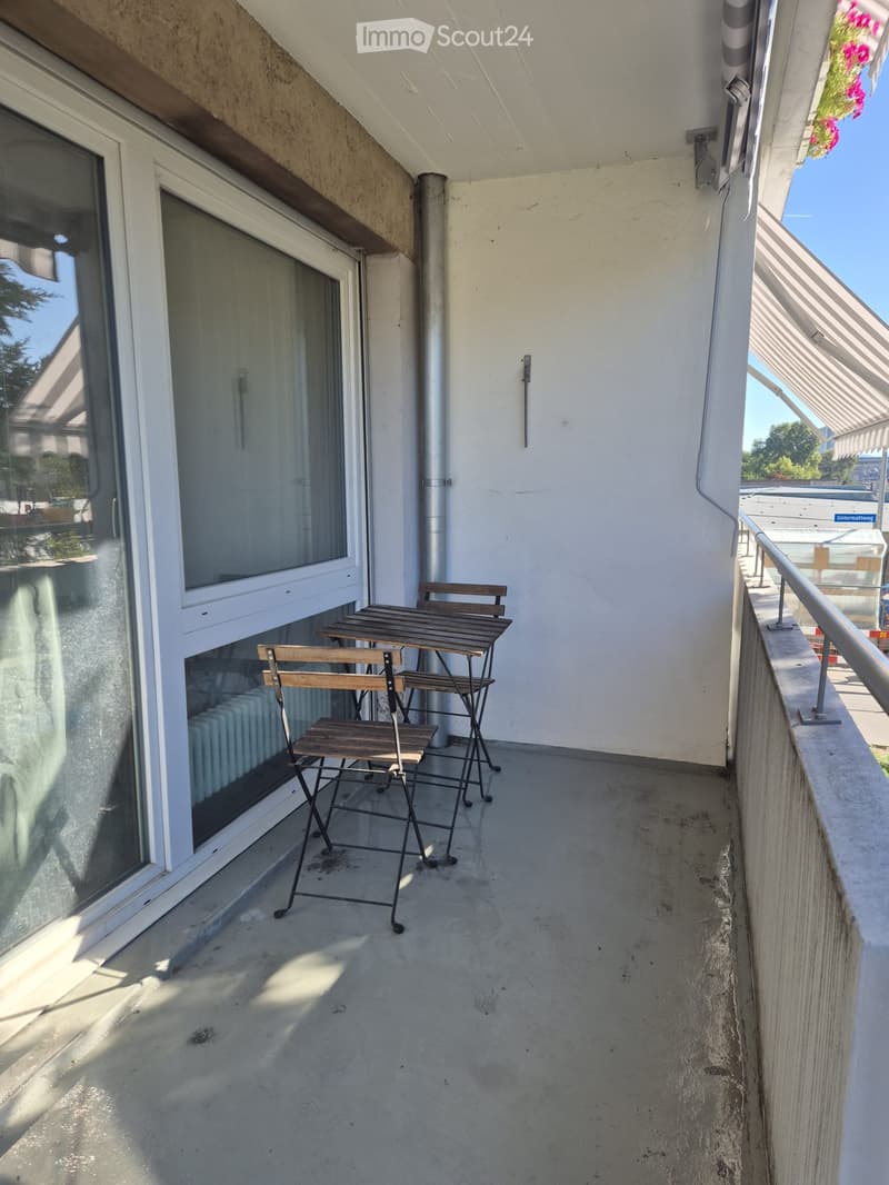 Balcony with a small table and four chairs, large windows, and a metal railing.