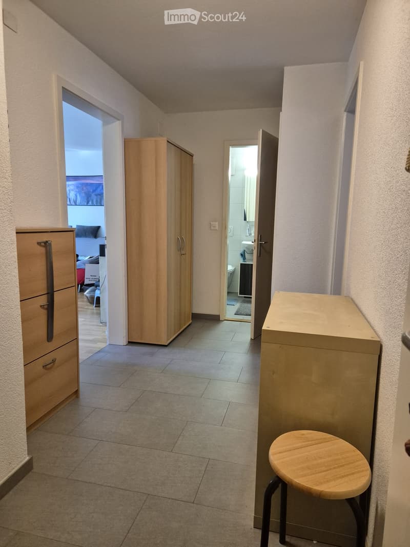 A narrow hallway with tiled flooring, light-colored walls, and several doors leading to different rooms, including a bathroom and a bedroom.
