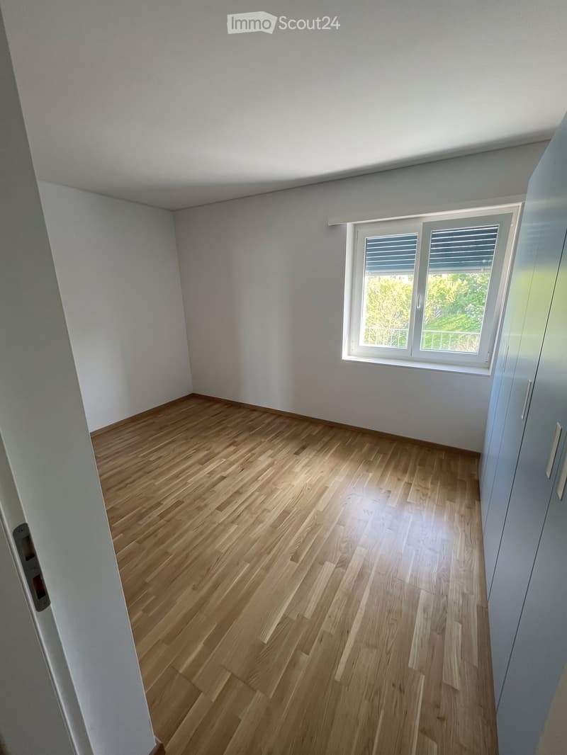 Empty room with light wooden flooring, white walls, and a large window with blinds. No furniture or equipment is present.