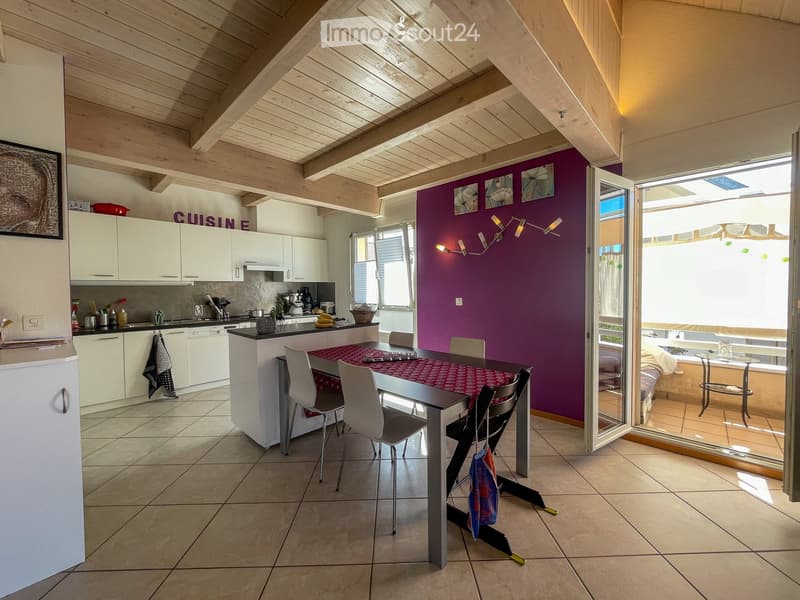 Modern kitchen with white cabinets, a central island, and a dining area. The space features a purple accent wall, exposed wooden beams, and large windows with blinds.