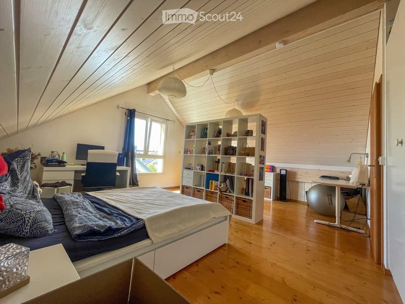 Bright attic bedroom with wooden floors and slanted ceilings, featuring a bed, desk, bookshelf, and exercise ball.