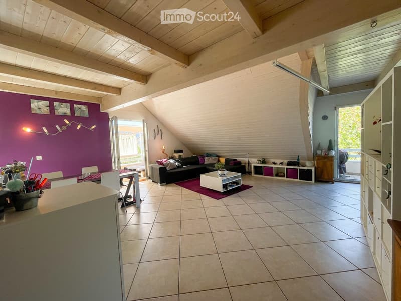 Bright living room with exposed wooden beams, purple accent wall, and large windows. Features a black sectional sofa, white coffee table, dining area with chairs, and built-in storage units.