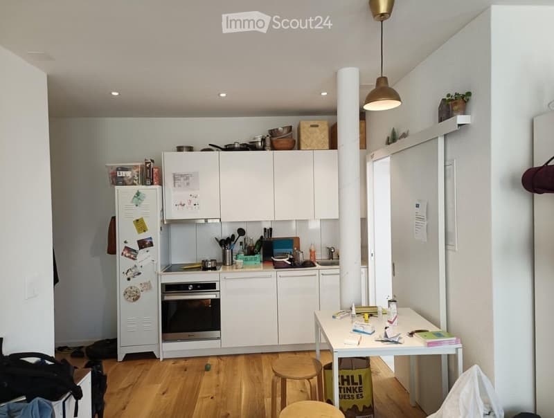 Modern kitchen with white cabinets, stainless steel appliances, wooden flooring, and a small dining area with a table and stools.