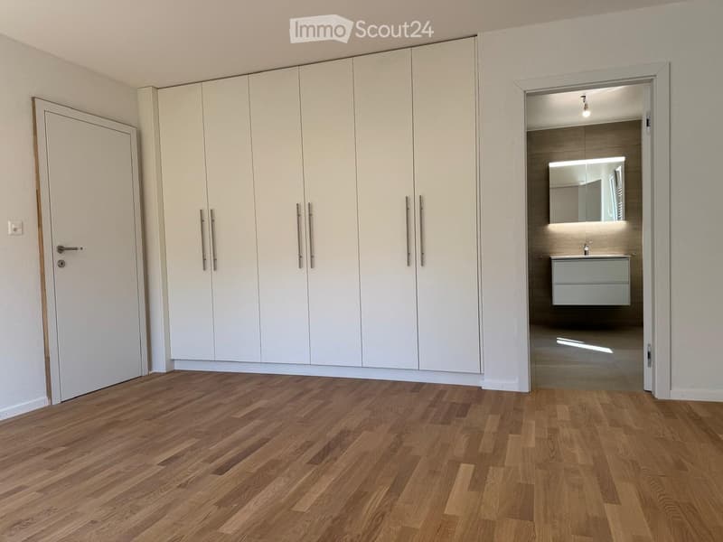 Empty room with light-colored wooden flooring, white built-in wardrobes, and an open doorway leading to a modern bathroom.