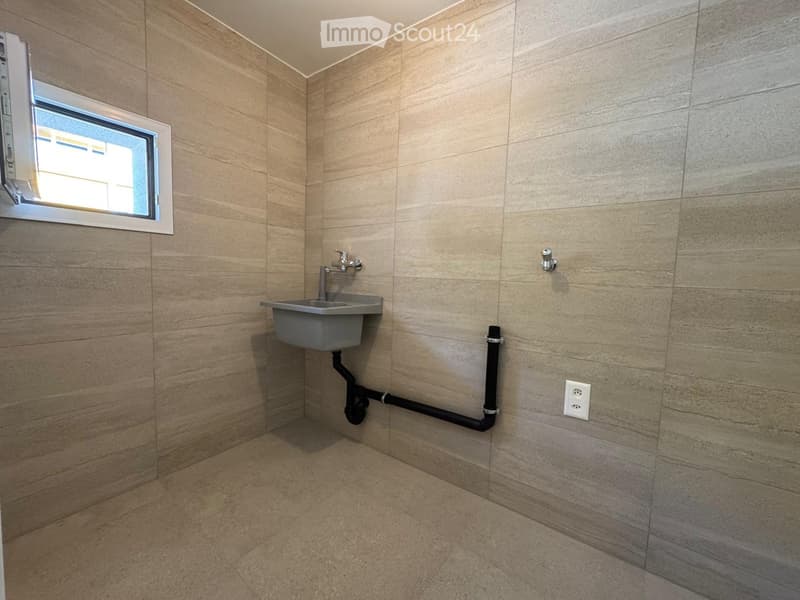 Modern bathroom with beige tiled walls and floor, a single sink with a modern faucet, a small window, and a visible electrical outlet.