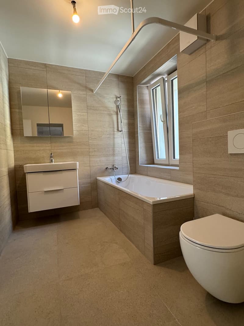 Modern bathroom with beige tiles, a bathtub, toilet, sink, and a mirrored cabinet.