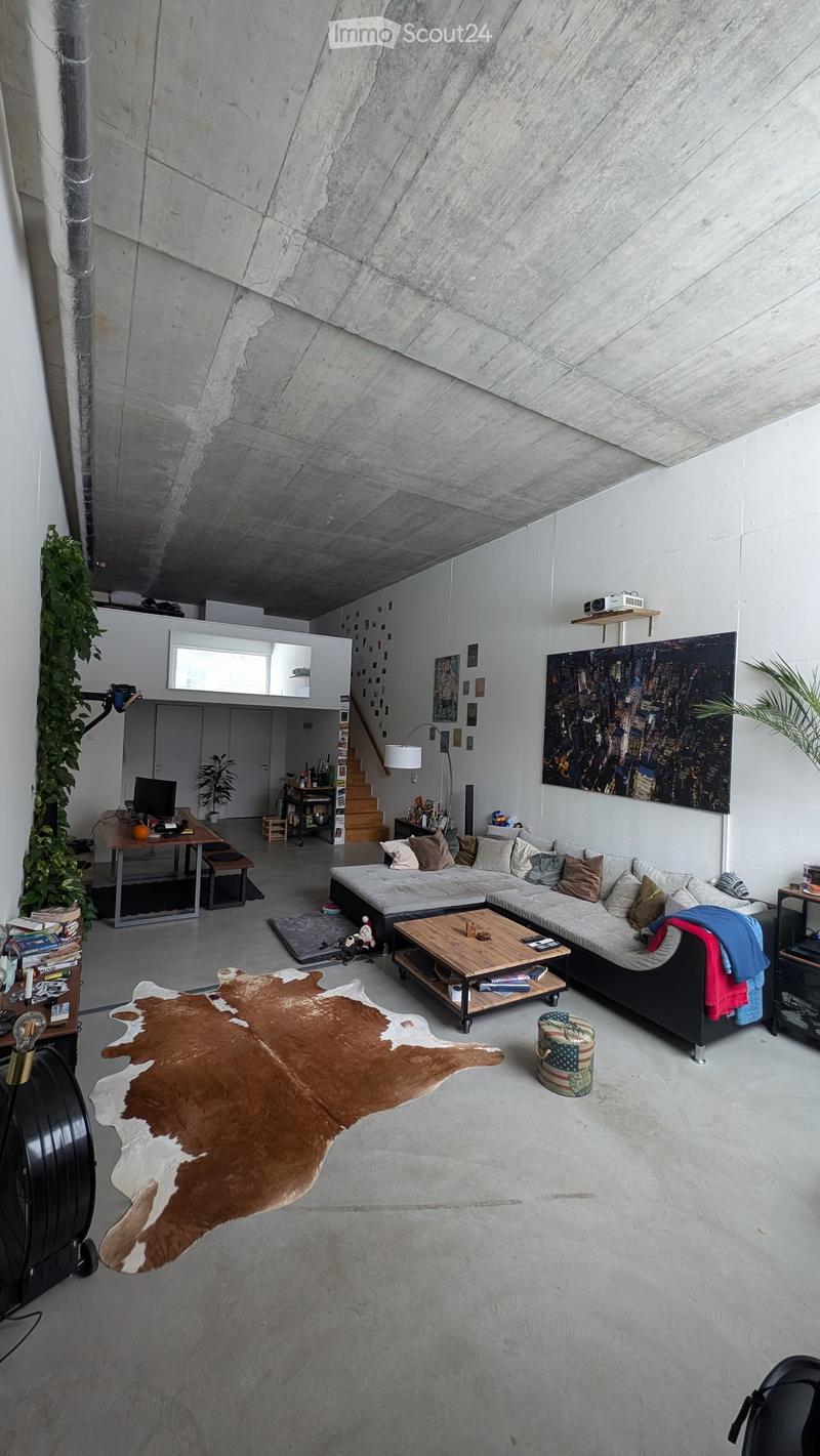 Modern living room with exposed concrete walls and ceiling, featuring a large sectional sofa, coffee table, and a cowhide rug on the floor.