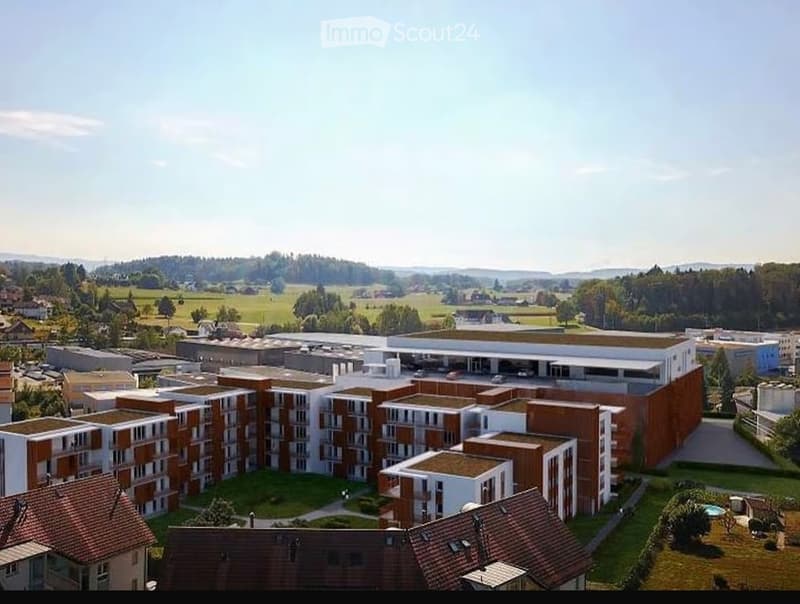 Aerial view of a modern residential complex with multiple apartment buildings, surrounded by green spaces and a parking area.