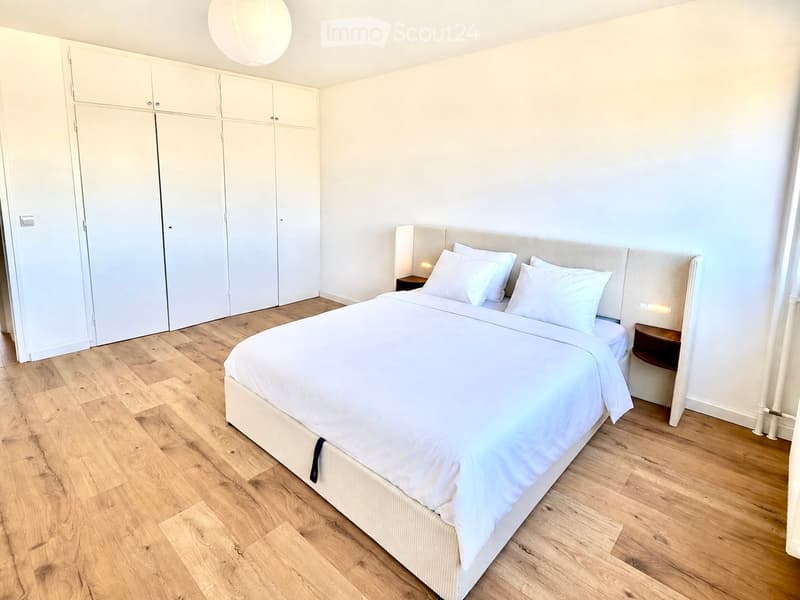 Modern bedroom with a large double bed, white bedding, wooden flooring, built-in wardrobes, and bedside tables.