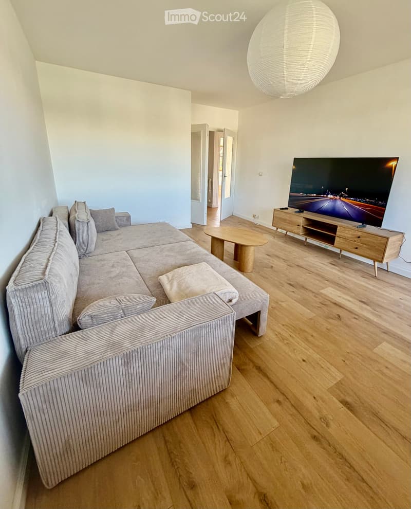 Modern living room with a grey sectional sofa, wooden coffee table, TV stand, and a large hanging lamp.