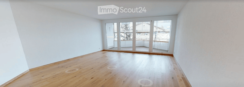 Empty room with wooden flooring, white walls, and large glass doors leading to a balcony.