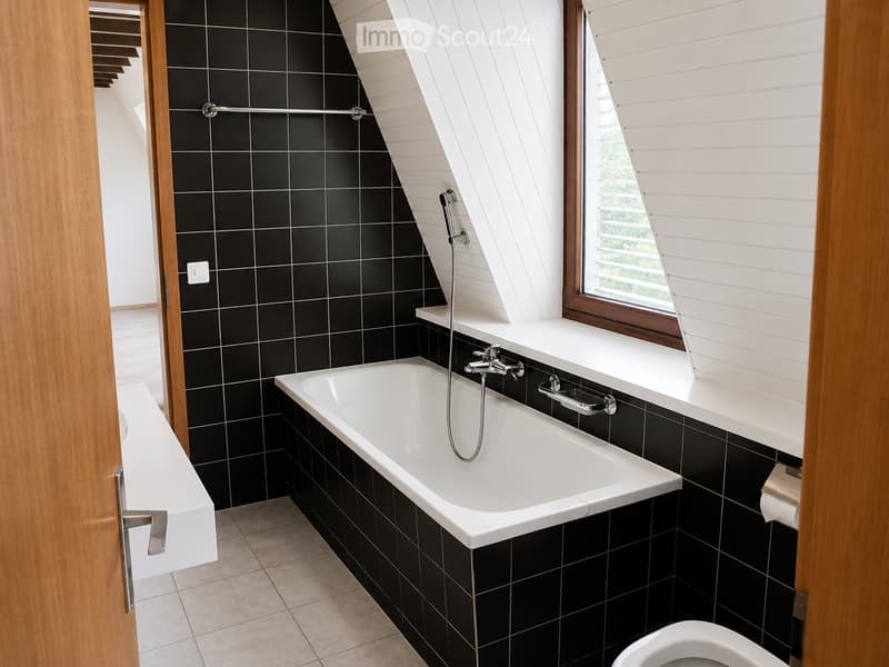 Modern bathroom with black tiled walls, a white bathtub, a toilet, a sink, and a window with wooden shutters.