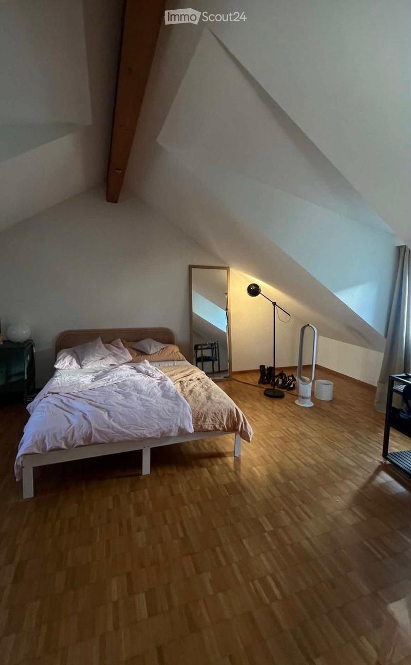 Cozy attic bedroom with wooden flooring, a single bed with white bedding, a large mirror, a floor lamp, and a nightstand.