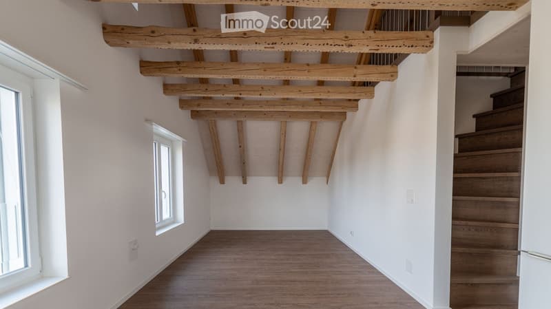 Empty hallway with exposed wooden beams on the ceiling, wooden flooring, and a staircase leading upwards.