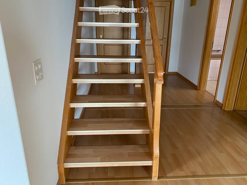 Wooden staircase with white handrails leading to an adjacent room with wooden flooring and a door.
