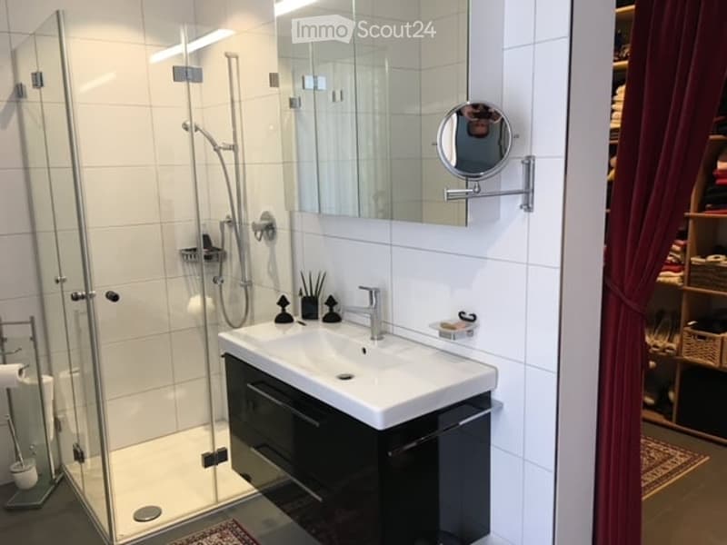 Modern bathroom with a white sink, chrome faucet, large mirror, glass-enclosed shower, and black cabinetry.