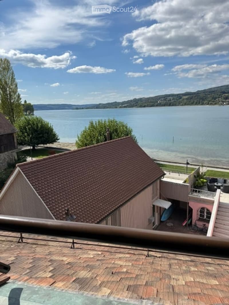 Balcony overlooking a lake with a view of the water and surrounding landscape, featuring a small seating area with chairs and a table.
