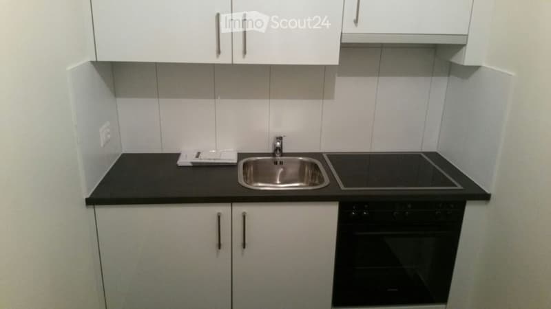 Modern kitchen with white cabinets, black countertops, a stainless steel sink, and a built-in oven.