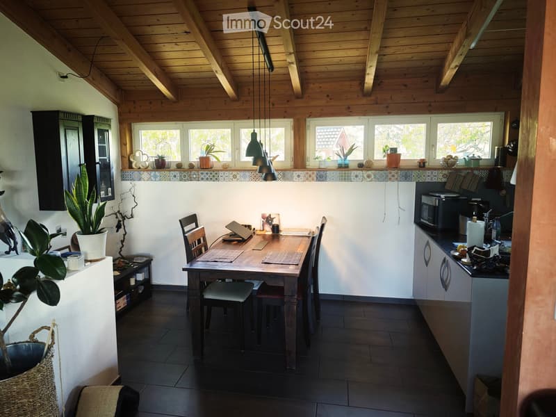 Open-plan kitchen and dining area with wooden beams, dark tiled floor, and modern kitchen appliances.