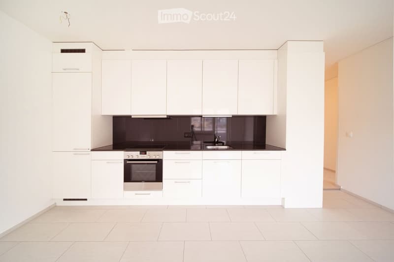 Modern kitchen with white cabinets, stainless steel oven, and sink, featuring a dark countertop and tiled floor.