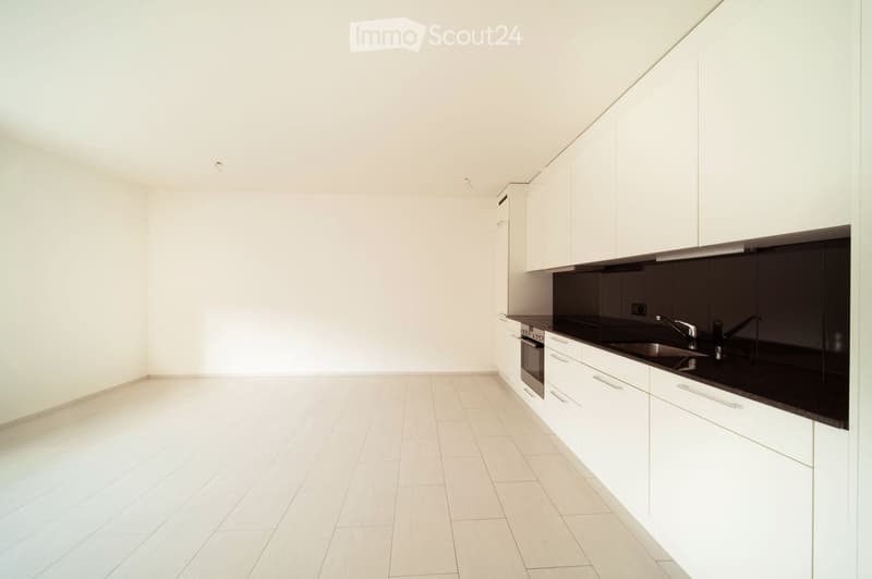 Empty kitchen with white cabinets, black countertops, and tiled flooring. No appliances or furniture are present.