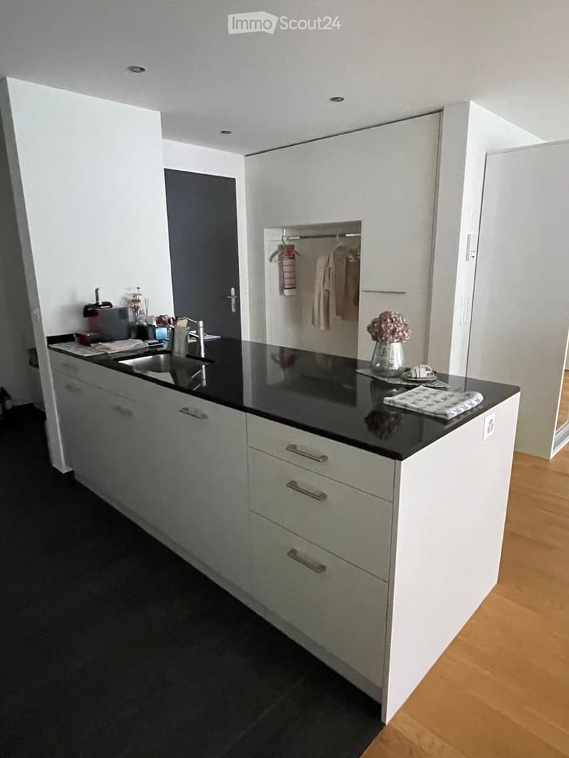 Modern kitchen with white cabinets, black countertop, sink, and small decorative items including a vase with flowers and a cup.