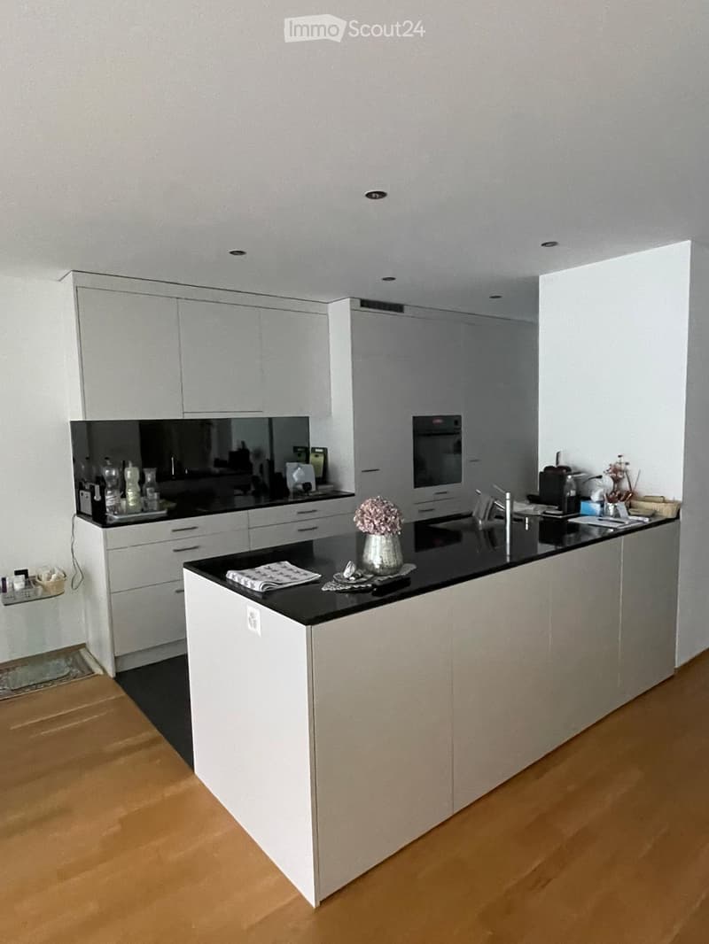 Modern kitchen with white cabinets, black countertops, and a central island. Features include a sink, faucet, oven, and decorative vase on the island.