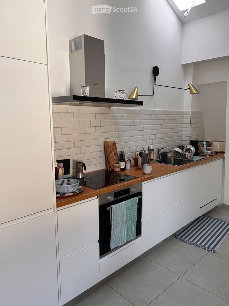 Modern kitchen with white cabinets, wooden countertops, stainless steel appliances, and various kitchen items on the counter.