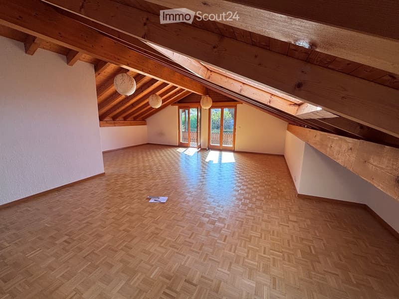 Empty attic room with wooden herringbone flooring, exposed wooden beams, and skylights. Two French doors lead to a balcony area.