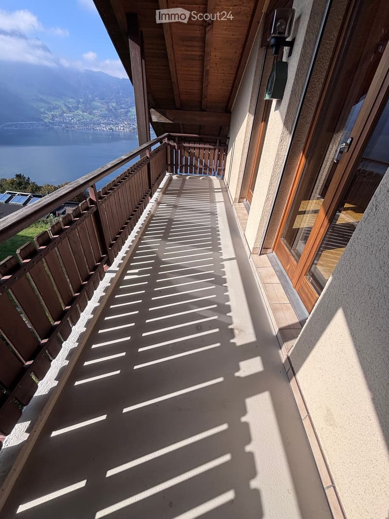 Balcony with wooden railing, tiled floor, and scenic mountain and lake view in the background.