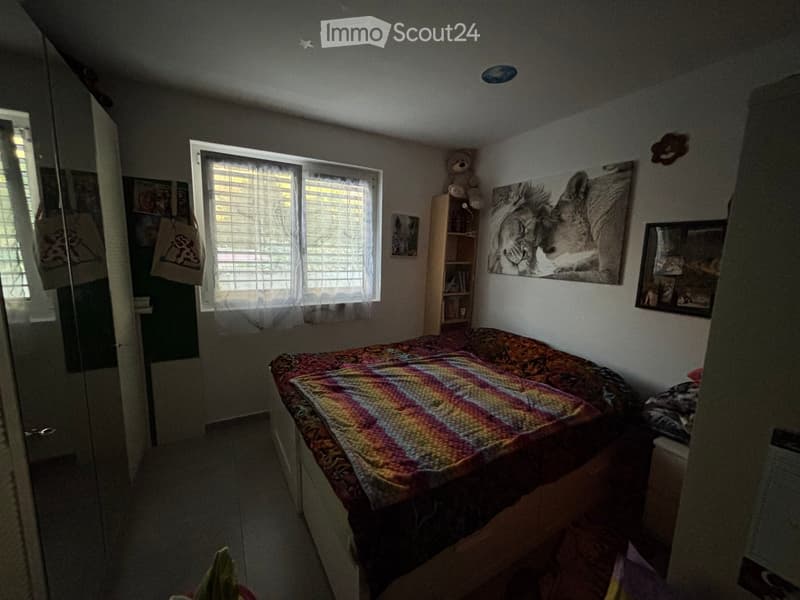 Bedroom with a single bed, colorful bedspread, nightstand, bookshelf, and wall decorations including a large animal print picture and framed photos.