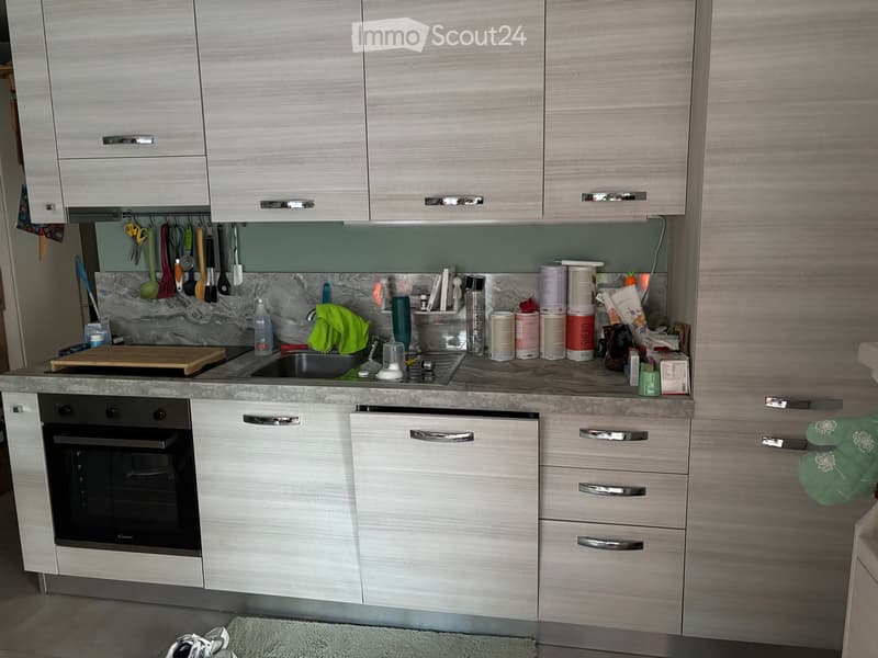 Modern kitchen with light wood cabinets, stainless steel appliances, marble backsplash, and various kitchen utensils and items on the counter.
