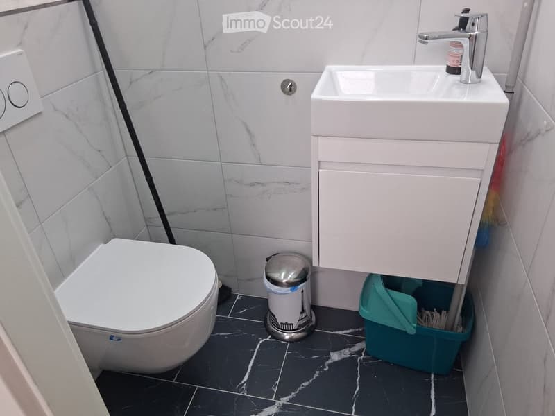 Modern bathroom with white marble tiles, a toilet, a sink with a chrome faucet, and a decorative trash can featuring the Eiffel Tower.