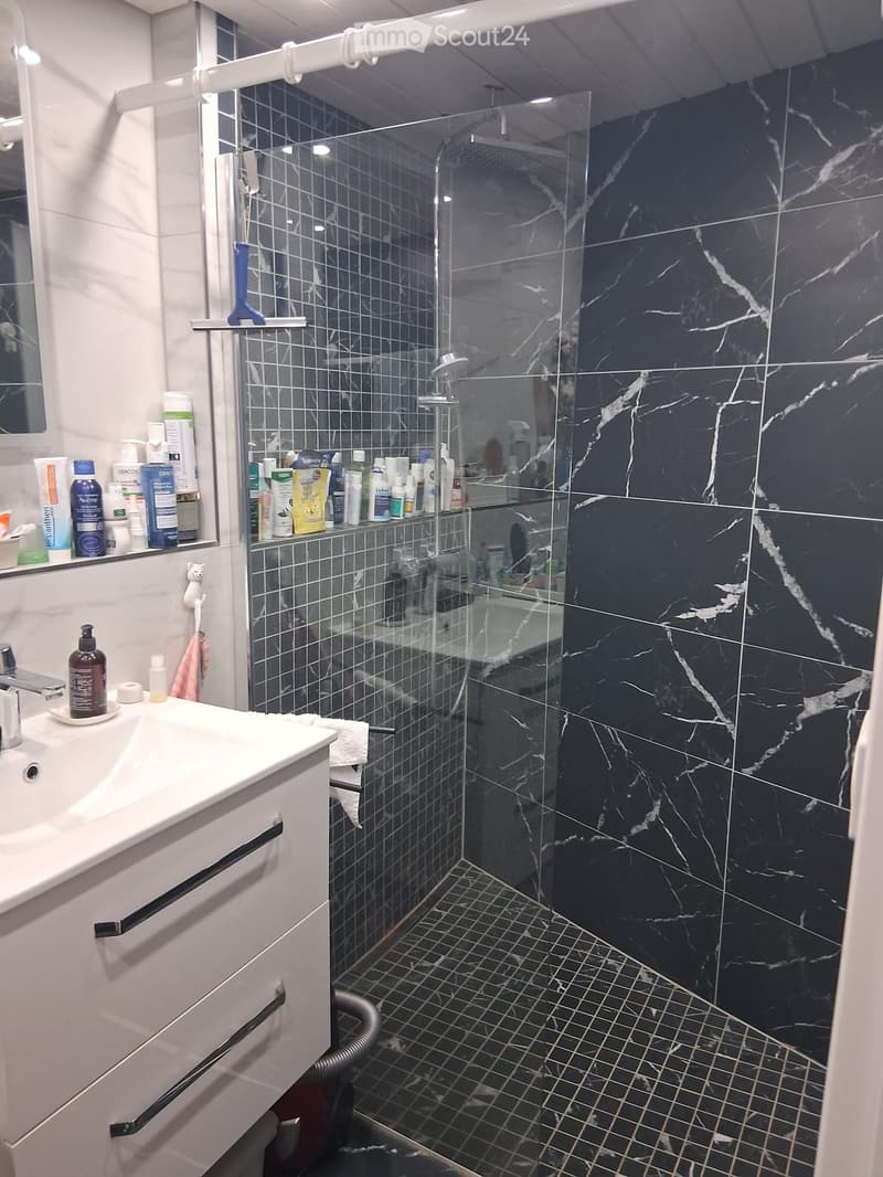 Modern bathroom with a white sink, chrome faucet, marble shower stall, and various toiletries on shelves.