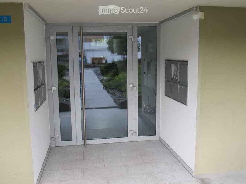 Modern hallway with glass double doors leading outside, mailboxes on either side, and a polished tile floor.