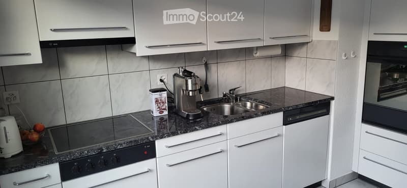 Modern kitchen with white cabinets, granite countertops, stainless steel appliances, and a coffee maker on the counter.