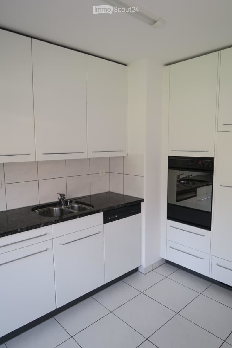 Modern kitchen with white cabinets, black granite countertops, stainless steel sink, dishwasher, and oven.