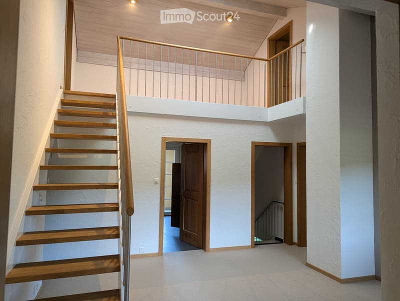Modern staircase with wooden steps and metal railing, leading to an upper level with white walls and wooden doors.