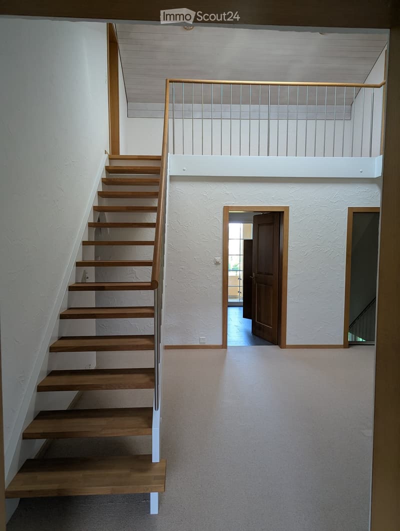 Wooden staircase with metal railing, white walls, and open doorway leading to another room.