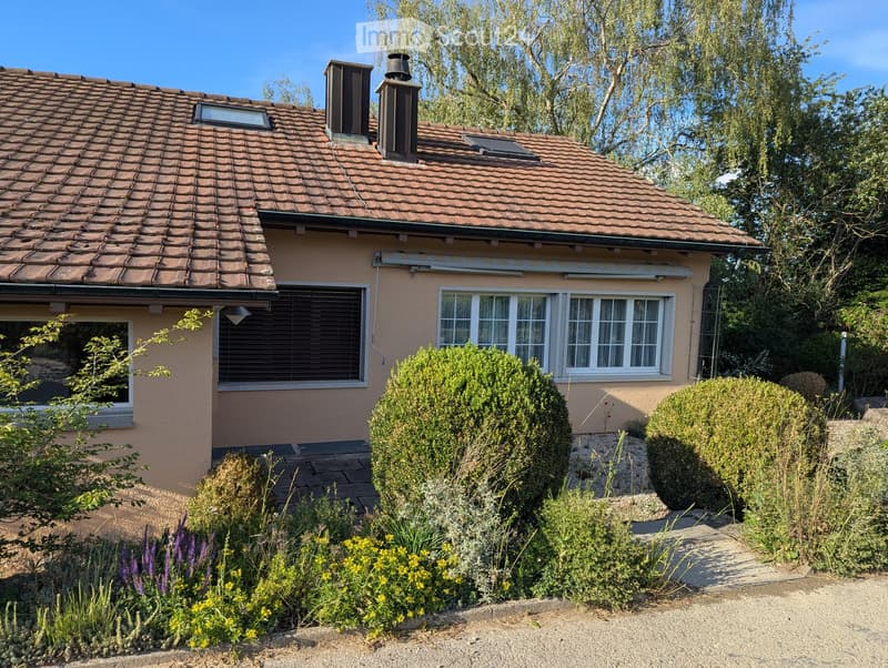 Two-story house with a tiled roof, multiple chimneys, and a well-maintained garden with shrubs and flowers.