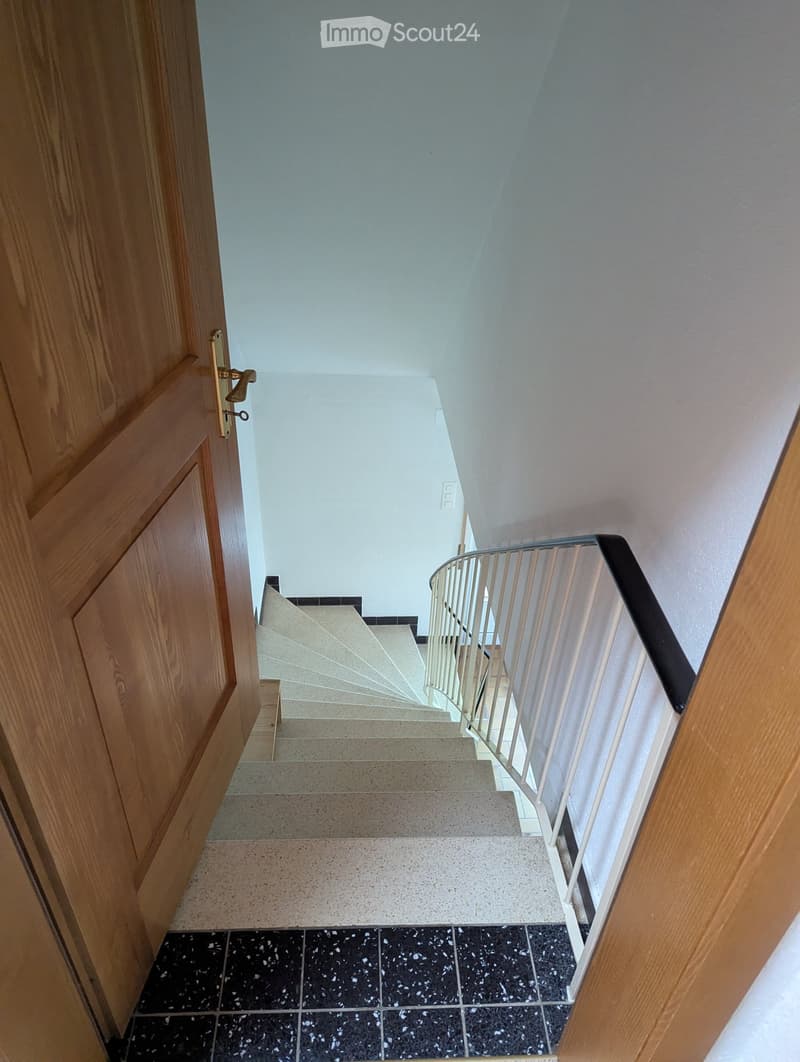 Spiral staircase with white walls and a wooden door on the left side.