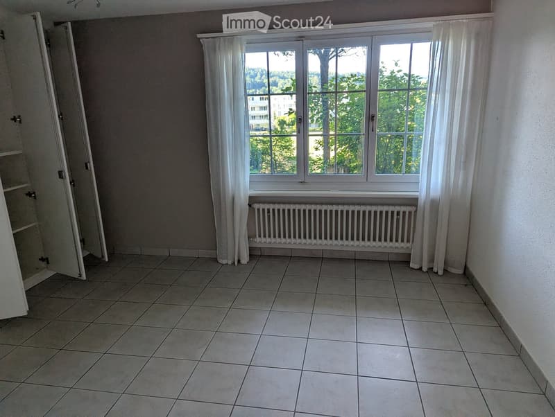 Empty room with tiled floor, large window with white curtains, radiator, and open closet door.
